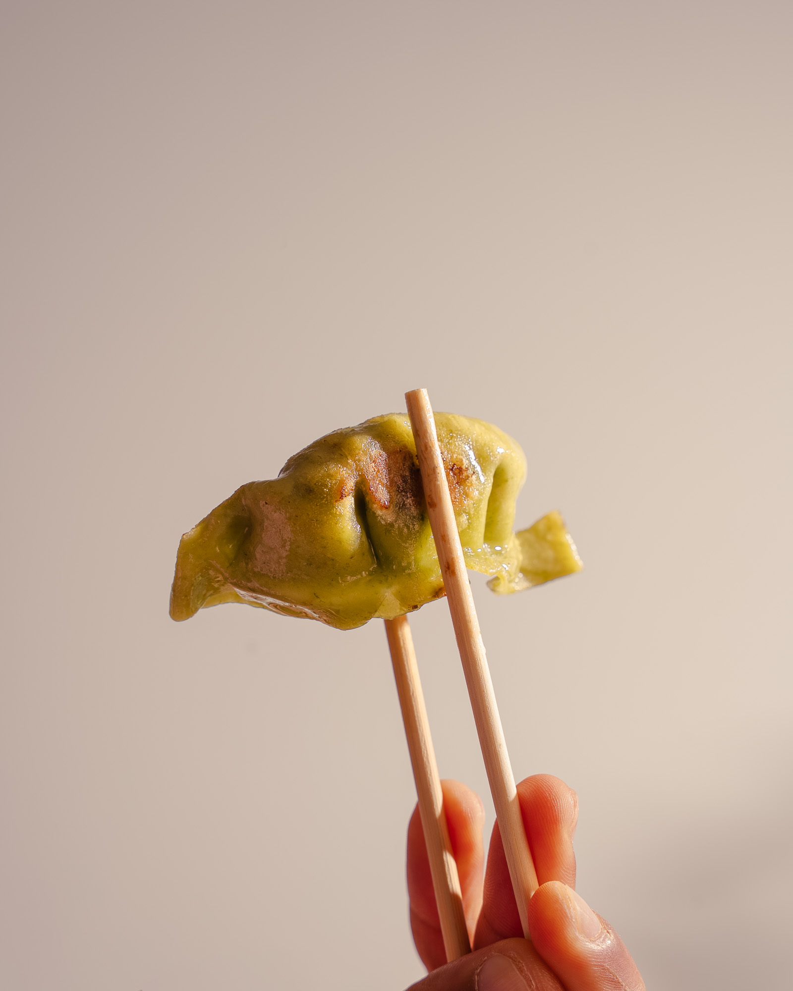 A single pan-fried green gyoza held with chopsticks