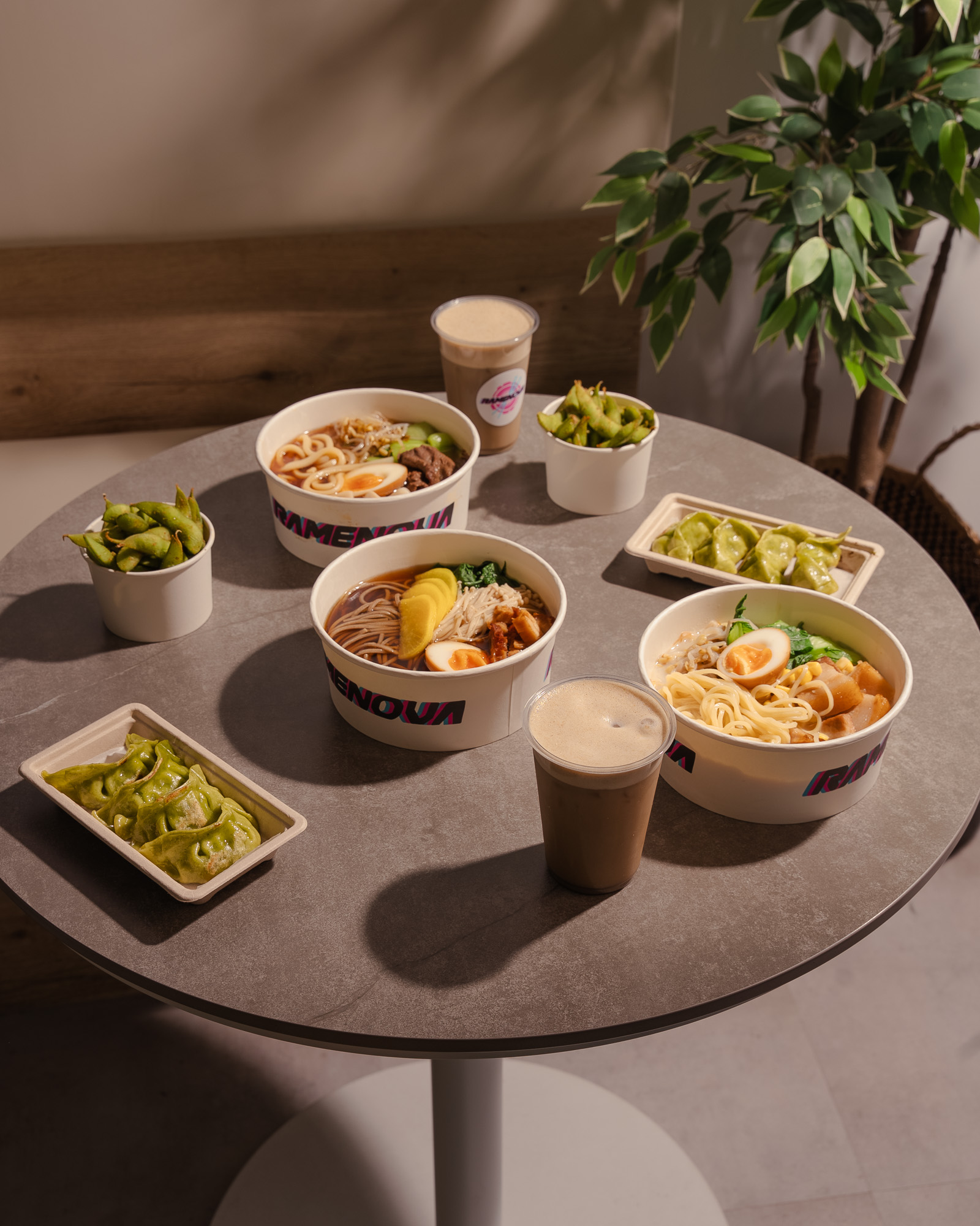 Ramenova bowls, gyoza, edamame and iced drinks on a table